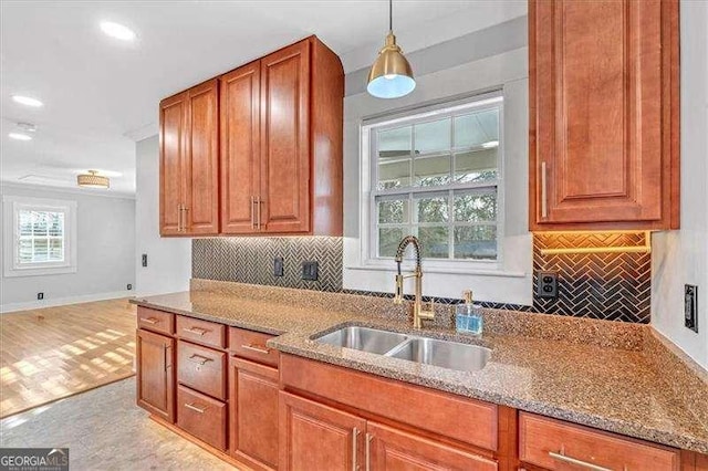 kitchen with decorative backsplash, light stone counters, hanging light fixtures, and sink