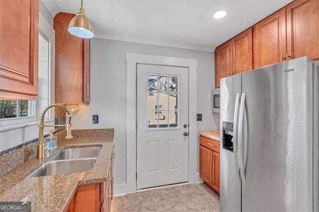 kitchen with stainless steel appliances, hanging light fixtures, crown molding, light stone counters, and sink