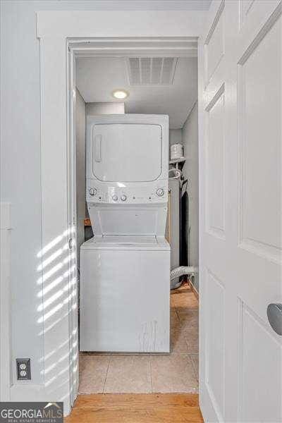 clothes washing area featuring light tile patterned flooring and stacked washer / dryer