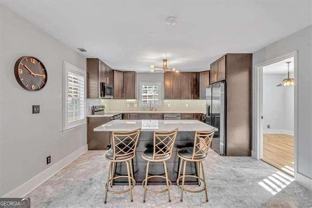 kitchen with tasteful backsplash, a notable chandelier, a kitchen island, a kitchen bar, and appliances with stainless steel finishes