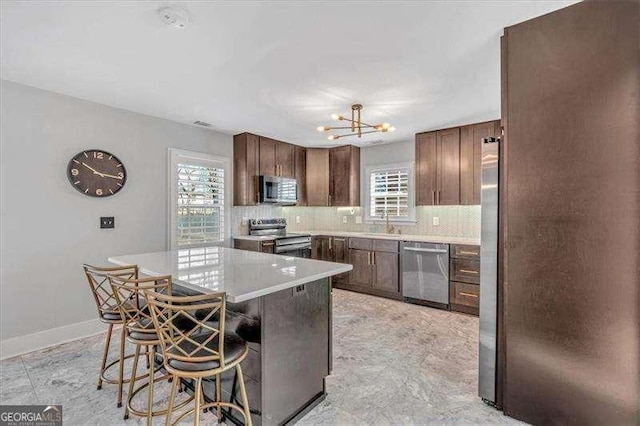 kitchen with appliances with stainless steel finishes, decorative backsplash, a notable chandelier, a breakfast bar, and sink