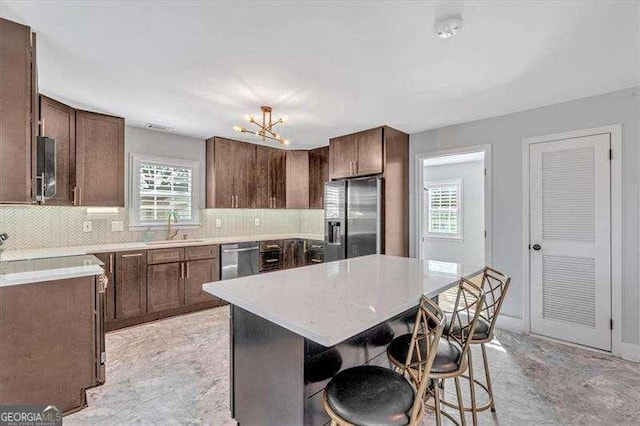 kitchen with a kitchen island, decorative backsplash, sink, appliances with stainless steel finishes, and a kitchen breakfast bar