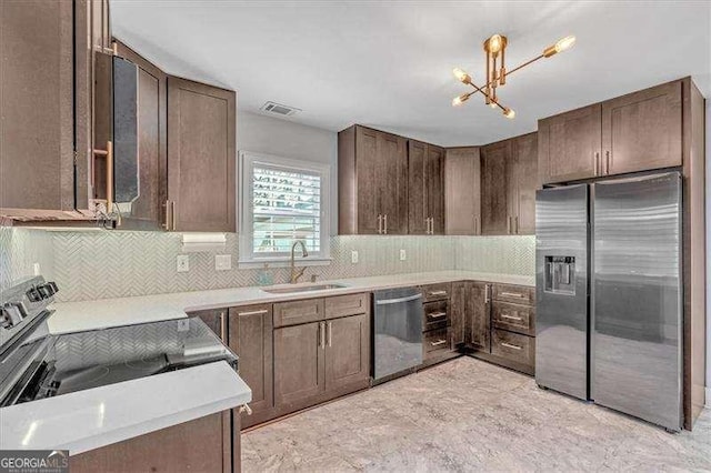 kitchen with dark brown cabinets, appliances with stainless steel finishes, sink, and a notable chandelier