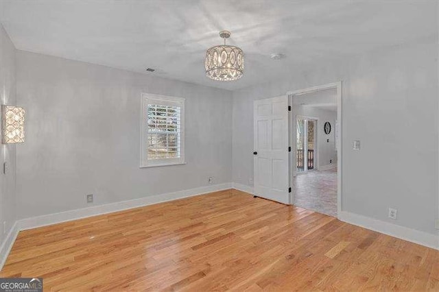 unfurnished room with light wood-type flooring and a notable chandelier