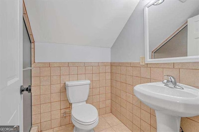 bathroom featuring lofted ceiling, toilet, tile walls, and sink