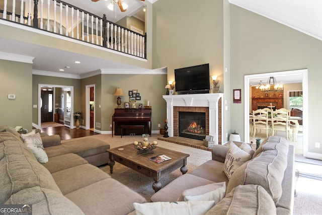 living room featuring a brick fireplace, a high ceiling, ornamental molding, and ceiling fan with notable chandelier