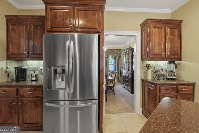 kitchen featuring stainless steel refrigerator with ice dispenser, crown molding, light carpet, and dark stone counters