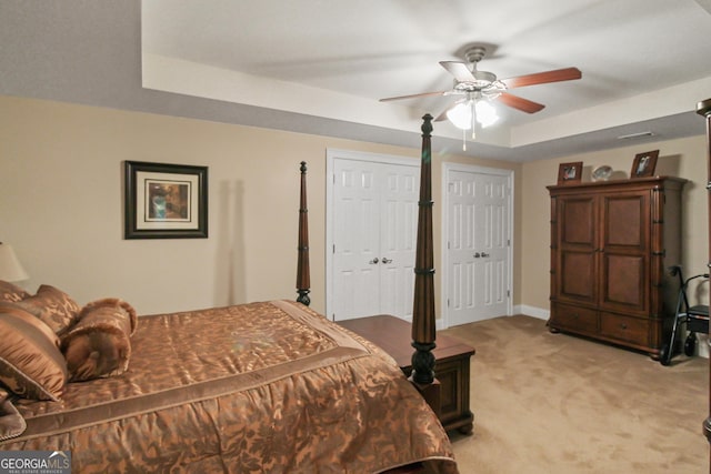 bedroom with ceiling fan, light colored carpet, and a tray ceiling