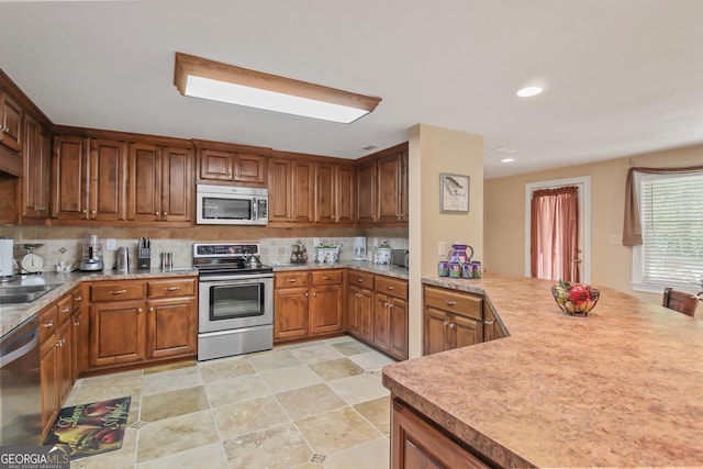 kitchen with sink, backsplash, appliances with stainless steel finishes, and kitchen peninsula