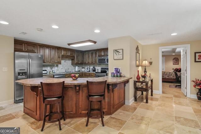 kitchen featuring a breakfast bar area, stainless steel appliances, kitchen peninsula, and backsplash