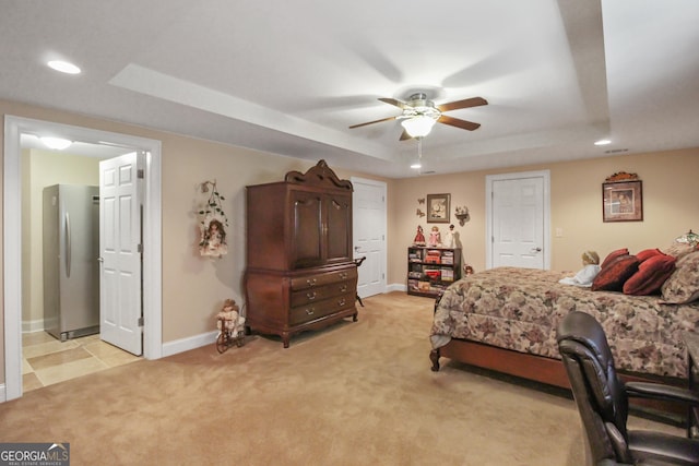 carpeted bedroom with ceiling fan, stainless steel refrigerator, and a tray ceiling