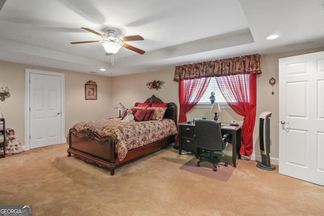 bedroom with ceiling fan, light colored carpet, and a tray ceiling