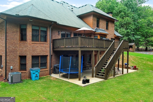 rear view of property featuring a trampoline, a patio area, a lawn, central AC, and a wooden deck