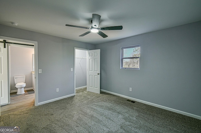 unfurnished bedroom featuring carpet floors, connected bathroom, a closet, ceiling fan, and a barn door