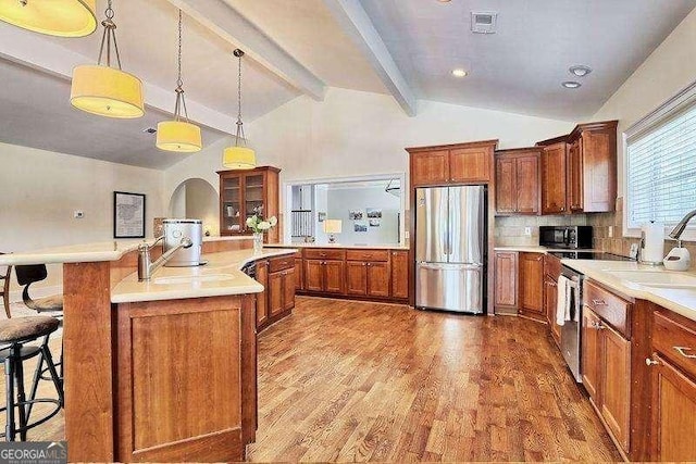 kitchen with pendant lighting, appliances with stainless steel finishes, decorative backsplash, lofted ceiling with beams, and a breakfast bar area