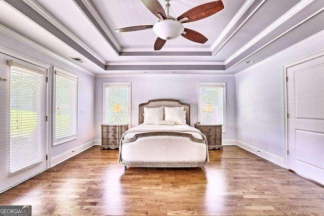 unfurnished bedroom featuring ceiling fan, access to exterior, a tray ceiling, and multiple windows