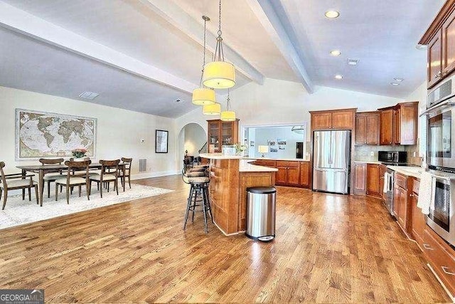 kitchen featuring wood finished floors, a breakfast bar, arched walkways, appliances with stainless steel finishes, and brown cabinets