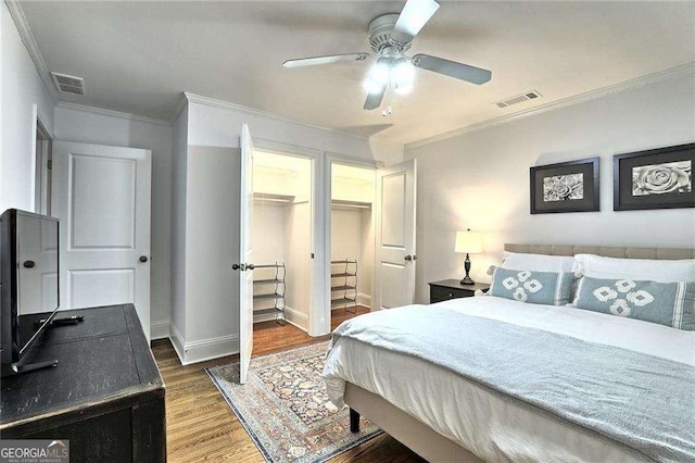 bedroom with a spacious closet, dark wood-type flooring, a closet, ceiling fan, and crown molding