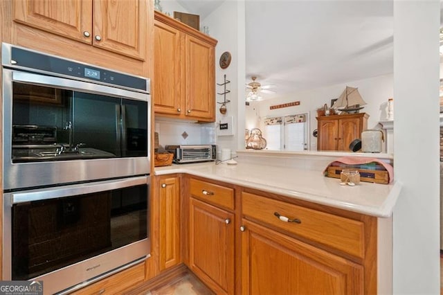 kitchen with tasteful backsplash, stainless steel double oven, kitchen peninsula, and ceiling fan