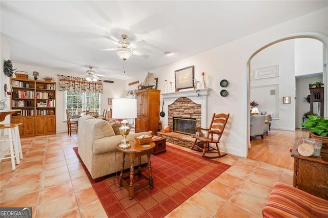 living room with ceiling fan, light tile patterned flooring, and a stone fireplace