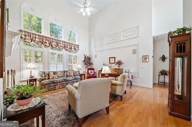 living room with ceiling fan, a towering ceiling, and light hardwood / wood-style flooring