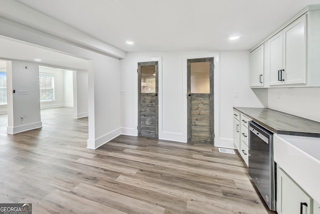 kitchen with white cabinets, vaulted ceiling, dishwasher, and light hardwood / wood-style flooring