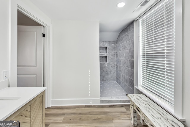 bathroom featuring wood-type flooring, tiled shower, and vanity