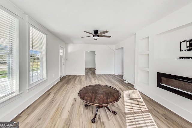 living room featuring light wood-type flooring, ceiling fan, and built in features