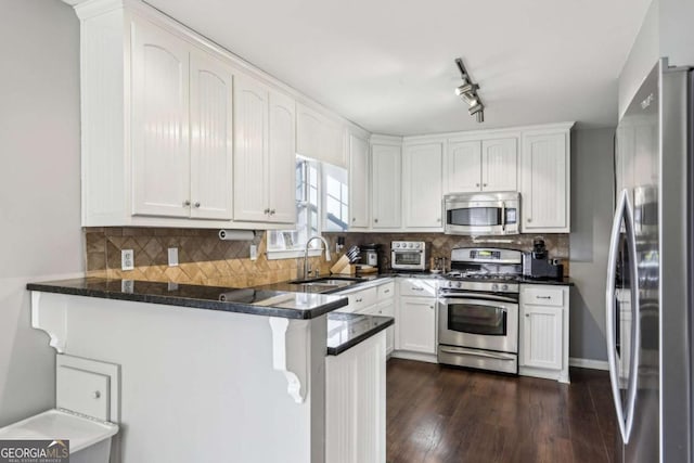 kitchen with kitchen peninsula, stainless steel appliances, backsplash, white cabinets, and sink