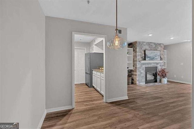 kitchen featuring white cabinetry, a stone fireplace, wood-type flooring, hanging light fixtures, and stainless steel refrigerator