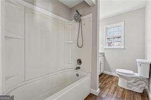 bathroom with hardwood / wood-style flooring, shower / bathing tub combination, and toilet