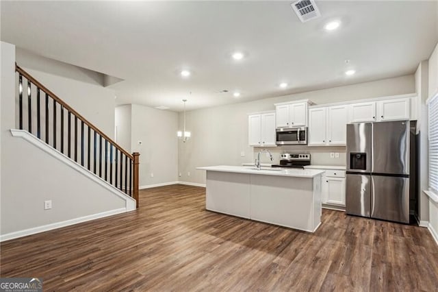 kitchen featuring white cabinets, appliances with stainless steel finishes, dark wood-type flooring, hanging light fixtures, and a kitchen island with sink