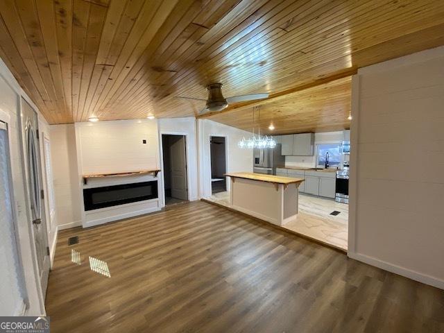 unfurnished living room with lofted ceiling, wood ceiling, wood finished floors, a fireplace, and a sink