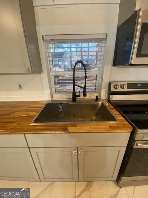 kitchen featuring stainless steel range with electric stovetop, butcher block counters, white cabinetry, and a sink