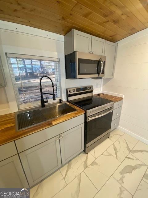kitchen with baseboards, a sink, stainless steel appliances, marble finish floor, and wooden ceiling