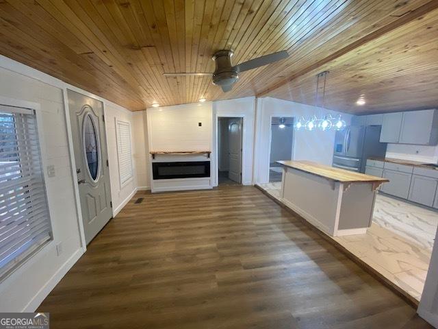 unfurnished living room featuring ceiling fan, dark wood-type flooring, wooden ceiling, lofted ceiling, and baseboards