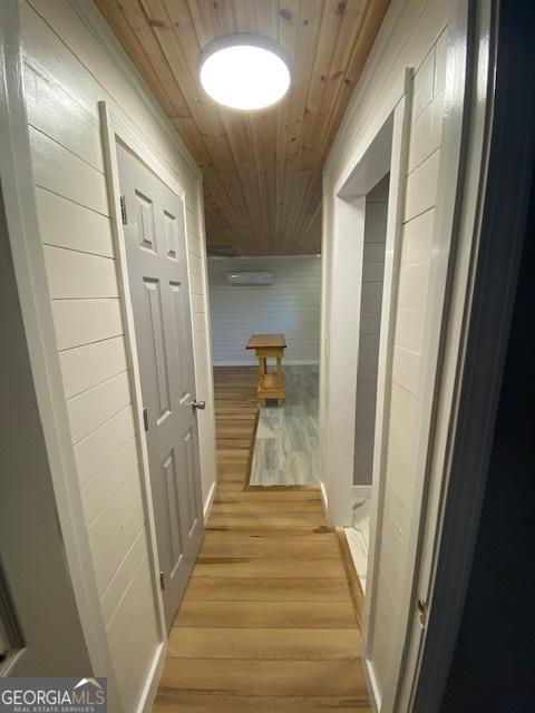 hall with light hardwood / wood-style flooring, wood walls, and wood ceiling