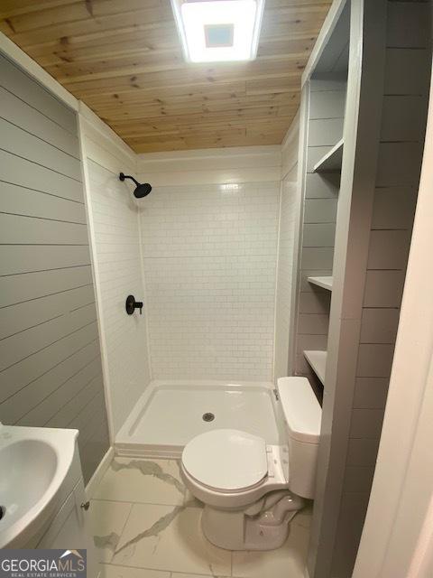 full bathroom featuring wood walls, toilet, a shower stall, and marble finish floor
