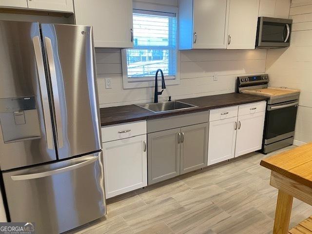 kitchen featuring stainless steel appliances, white cabinets, a sink, and backsplash