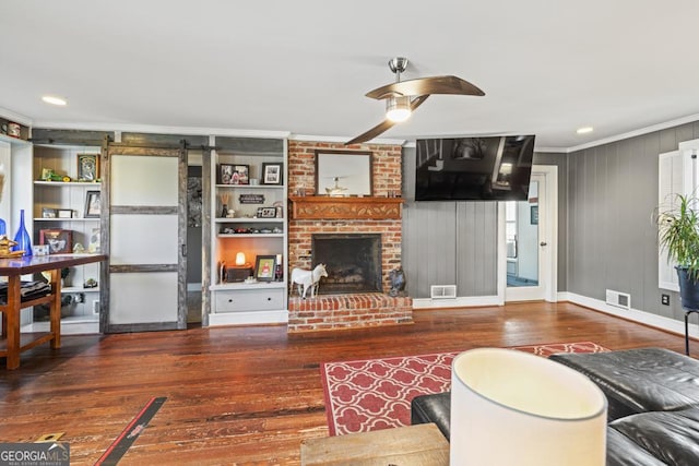 living room featuring a fireplace, crown molding, wood-type flooring, ceiling fan, and a barn door