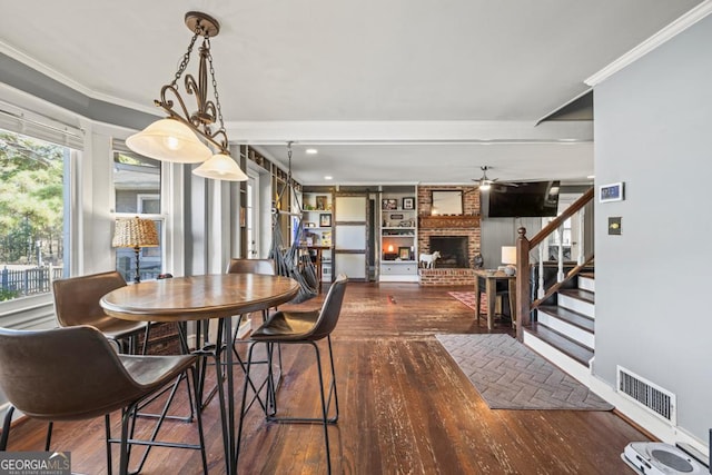 dining room with dark hardwood / wood-style flooring, crown molding, ceiling fan, and a fireplace