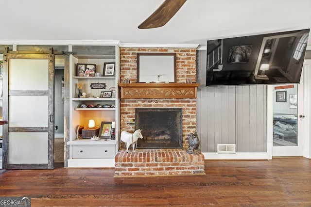 living room with ornamental molding, a barn door, a fireplace, and dark hardwood / wood-style flooring