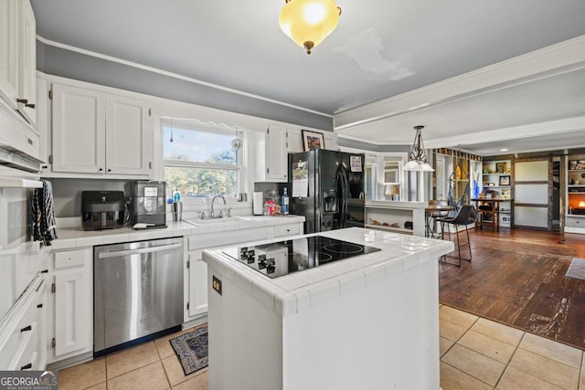 kitchen featuring hanging light fixtures, a center island, tile counters, black appliances, and white cabinets