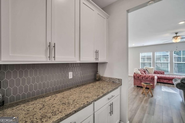 kitchen with ceiling fan, tasteful backsplash, light wood-type flooring, light stone countertops, and white cabinets