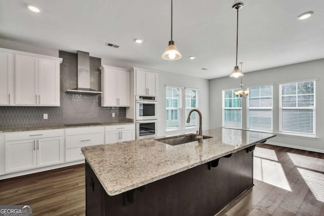 kitchen with double oven, wall chimney exhaust hood, sink, and a large island