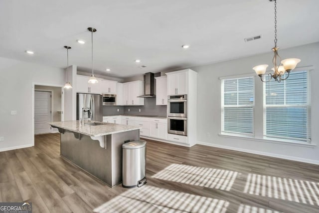 kitchen with white cabinetry, a kitchen bar, stainless steel appliances, decorative light fixtures, and wall chimney range hood