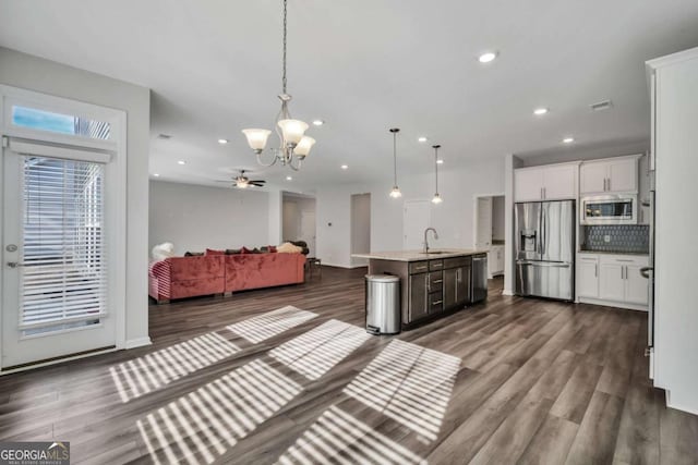 kitchen with pendant lighting, appliances with stainless steel finishes, tasteful backsplash, sink, and a center island with sink