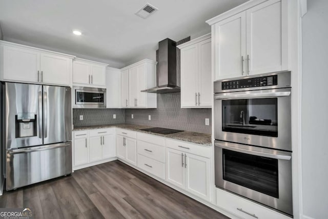 kitchen featuring appliances with stainless steel finishes, white cabinets, light stone counters, and wall chimney range hood