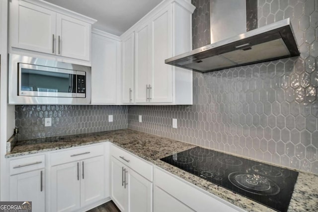 kitchen featuring backsplash, wall chimney range hood, black electric stovetop, and white cabinetry