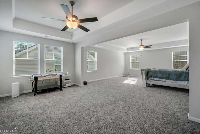 carpeted bedroom with ceiling fan, a tray ceiling, and multiple windows